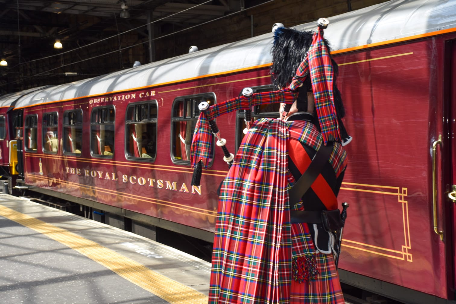 Scottish man playing bagpipes by the Belmond Royal Scotsman train